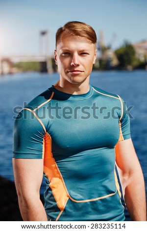 Young handsome male athlete wearing tight t-shirt is standing near the river