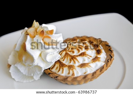 Lemon meringue pie & whipped cream: individual pie with meringue topping served with whipped cream on the side. Shot on black.