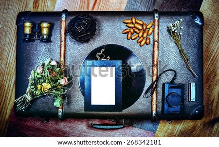 Vintage stylized Photo Frame mockup on suitcase. With vintage binoculars, rolling sone, acorn, rose, dry bouquet of flowers with roses, vinyl record, camera and twig. Suitcase have some scratches.