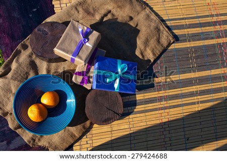 Orange on striped plate besides of gifts on wood background. Nature light.