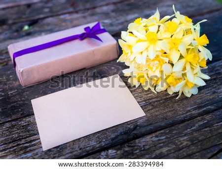 Bouquet of flowers Narcissuses on natural wood background with gift. Nature light.