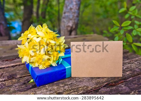 Bouquet of flowers Narcissuses on natural wood background with gift and envelope. Nature light.