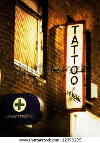 Tattoo and piercing sign outside tattoo parlor that is over a Pharmacy