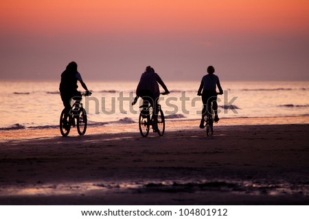 Three cyclists on the beach at sunset