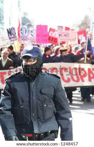 Riot police man in front of a crowd of angry protestors holding a banner that says occupation is a crime