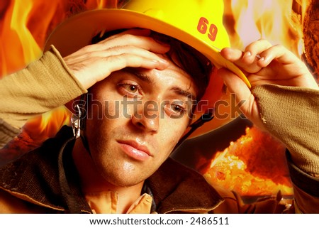 Vertical close-up of a firefighter in his gear wiping sweat from forehead with fire in background