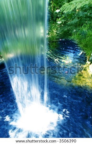 tropical waterfall with smooth edge and yellow and red flowers in the background of a garden view