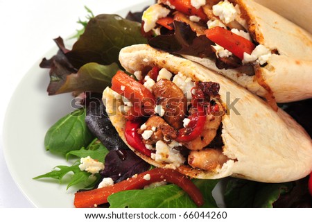 Pitta bread on salad leaves filled with a chicken, vegetables and feta cheese