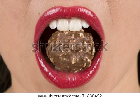 Macro of a beautiful woman holding chocolate candy with her teeth