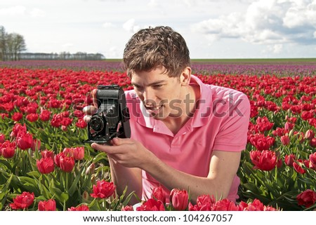 Young guy making a picture with an old fashioned camera in the countryside from the Netherlands