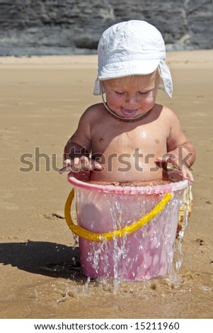 Cute little baby boy playing in a bucket full of water at the beach