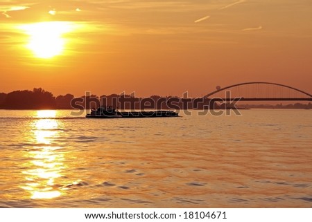 Freighter cruising on the river Merwede with the Moerdijkbrug in the Netherlands at sunset