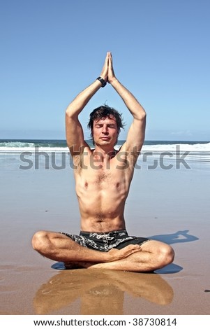Young handsome man meditating on the beach sitting in lotus position