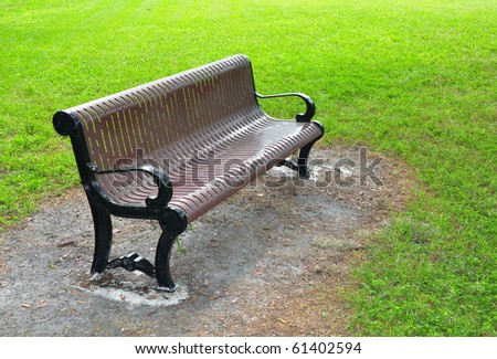 metal bench painted brown, surrounded by grass in a park..