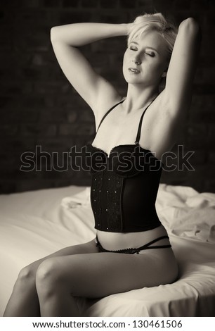 Beautiful and very sexy young adult caucasian woman in Black lingerie with blonde hair and blue eyes, in a bedroom setting with typical boudoir poses