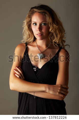 Beautiful young blonde caucasian woman with long curly honey blonde hair in a little black dress on a neutral background