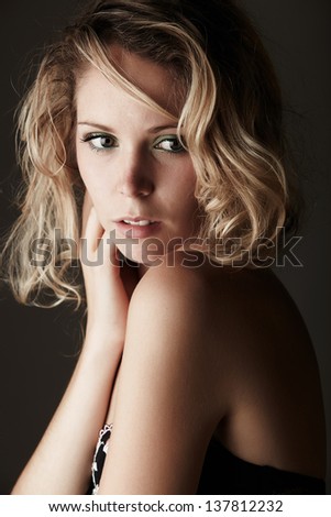 Beautiful young blonde caucasian woman with long curly honey blonde hair in black embroidered lingerie on a neutral background
