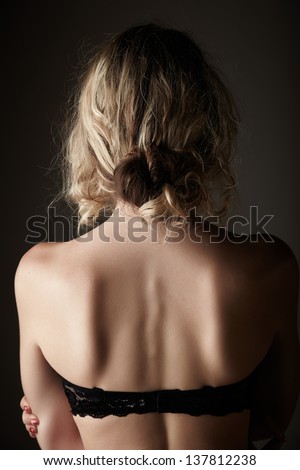 Beautiful young blonde caucasian woman with long curly honey blonde hair in black embroidered lingerie from behind on a neutral background