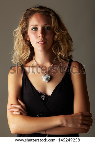 Beautiful young blonde caucasian woman with long curly honey blonde hair in a little black dress on a neutral background