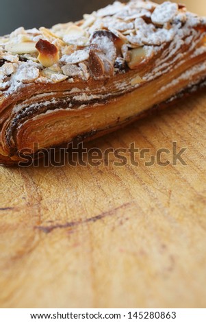Fresh chocolate and Almond rollover croissant pastry, sprinkled with icing sugar on a brown wooden serving board with copy space  - Shallow Depth of Field (DOF)