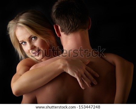 Young and fit caucasian adult couple in an embrace. Semi-nude and topless against a dark background .