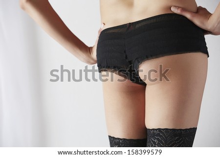 The bum of a sexy and beautiful young adult caucasian woman in black lingerie and stockings in a light white bedroom