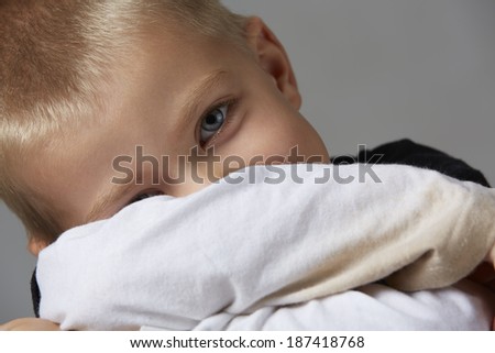 5 year old caucasian boy with short blonde hair, blue eyes and a light, healthy complexion wearing a long sleeve t-shirt. Shot in studio on a grey background.