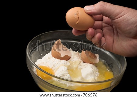 hand of a male breaking a egg into a glass bowl with cake flour in it, black background