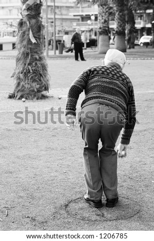 An old man playing petanque in Antibes, France.  Black and white.   Movement on person\'s right hand.  Copy space.