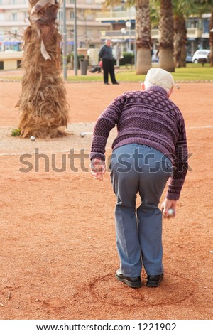 An old man playing petanque in Antibes, France.  Movement on person\'s right hand.  Copy space.