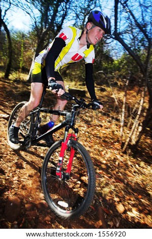 Panning shot of a mountain biker, racing in a forest.  Movement on background and some of the bike.  Face of biker in focus.