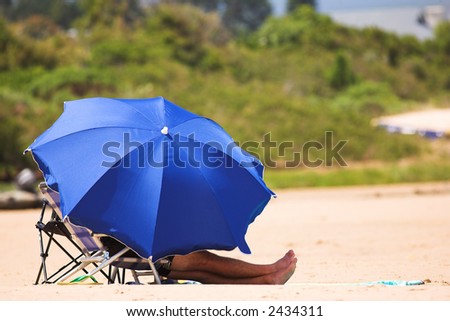 Man relaxing on the beach under a blue umbrella