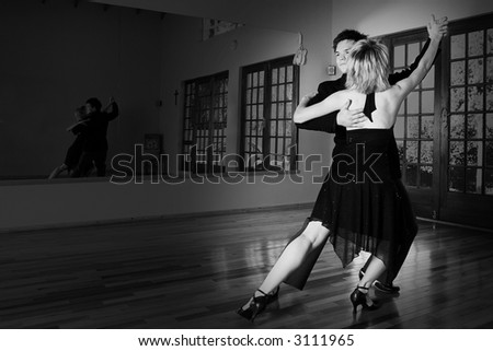 A young adult couple dancing and practicing ballroom dancing together in a studio - Focus on man, black and white image