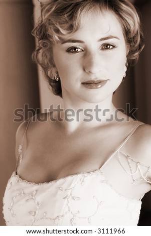 Young blonde bride with champagne colored wedding gown and red lips. She is looking over her shoulder with an alluring and seductive look in her green eyes. Duatone brown image (sepia tone)