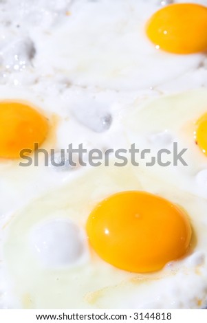 Fresh eggs being fried sunny side up on a large frying pan. Most of the egg white has already cooked. Shallow Depth of Field, focus on front egg