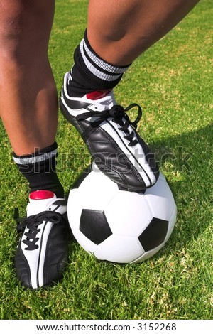A male soccer (football) player, referee or coach standing with one foot on a soccer ball. The image is of feet and legs, with soccer togs, and a black and white ball