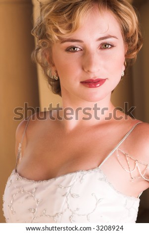 Young blonde bride with champagne colored wedding gown and red lips. She is looking over her shoulder with an alluring and seductive look in her green eyes. She is in a luxurious bedroom
