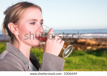 Young blonde Caucasian woman drinking wine next to the ocean wearing a business suit