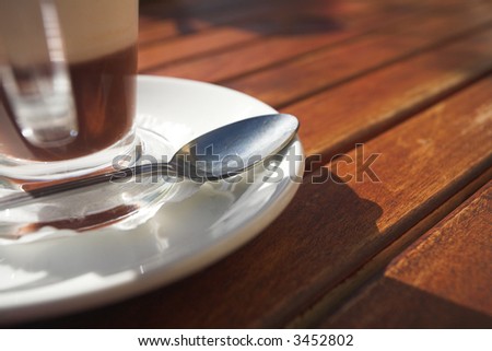 Glass coffee mug with rich coffee and foam on a brown wooden table – Shallow Depth of Field – focus on spoon
