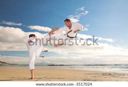 Young adult men practicing Karate on the beach. One is in a high kick and the other flying through the air (some movement on the edges)