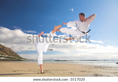 Young adult men practicing Karate on the beach. One is in a high kick and the other flying through the air (some movement on the edges)