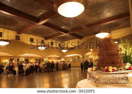 Layered chocolate wedding cake on a silver platter in the front of a wedding reception hall – Wide angle image – slight distortion on edges