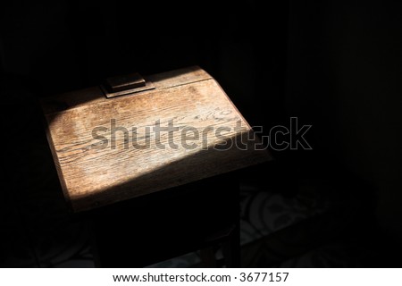 Old wooden pedestal standing empty inside a small chapel in a lone sunbeam from an open window