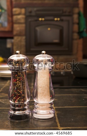 Salt and pepper shaker on a work surface inside a kitchen with a stove and oven in the background