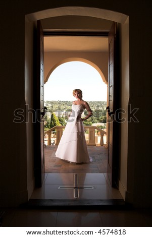 Young blonde bride with champagne colored wedding gown and red lips. She is standing outside the doorway on a porch