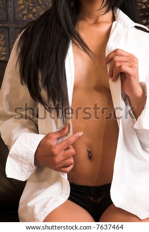Sexy adult Indian woman in black lace lingerie sitting on a brown leather couch with a white long sleeve shirt over her shoulders.