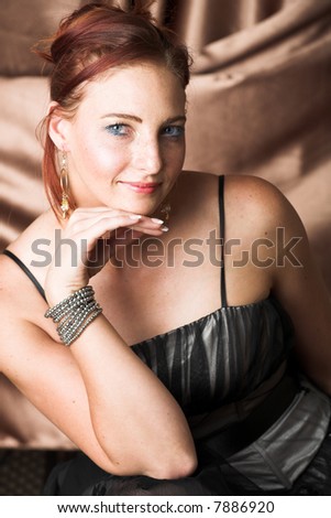 Young female adult fashion model with natural red hair and freckles in black chiffon evening wear with silver bracelet (Copper silk background) – hard light, high key image