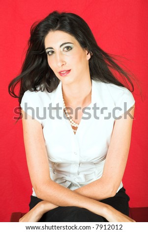 Beautiful young adult Italian businesswoman with long black hair, pearls and a white blouse on a textured red faux leather background