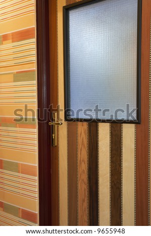 Wooden patterned door in brightly lit hallway with sharp downlights and soft brown carpets (perspective from wide angle lens)