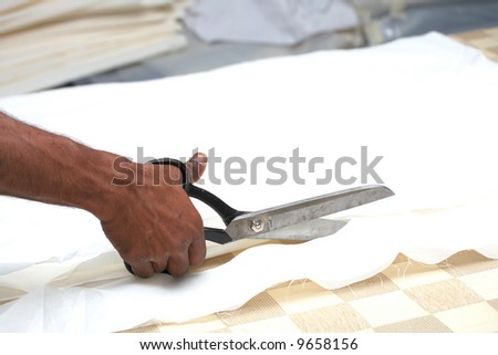 Man cutting white material with industrial sewing scissors, on a cutting table (Shallow Depth of Field ? focus on scissors)